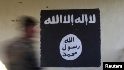  FILE - A soldier walks past a black flag commonly used by Islamic State militants. 