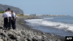 Police officers inspect metallic debris found on a beach in Saint-Denis on the French Reunion Island in the Indian Ocean on August 2, 2015, close to where a Boeing 777 wing part believed to belong to missing flight MH370 washed up last week.