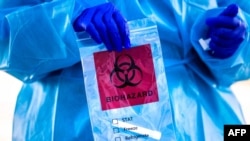 COVID Check Colorado site tester Pamela Deemie holds a bag after administering a COVID test at Echo Park Stadium on Dec. 30, 2020, in Parker, Colo.