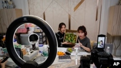 In this May 5, 2020, photo, China's online celebrity Zhang Mofan, right, introduces fresh mangos to her online clients and fans through the live-streaming at her house in Beijing. 