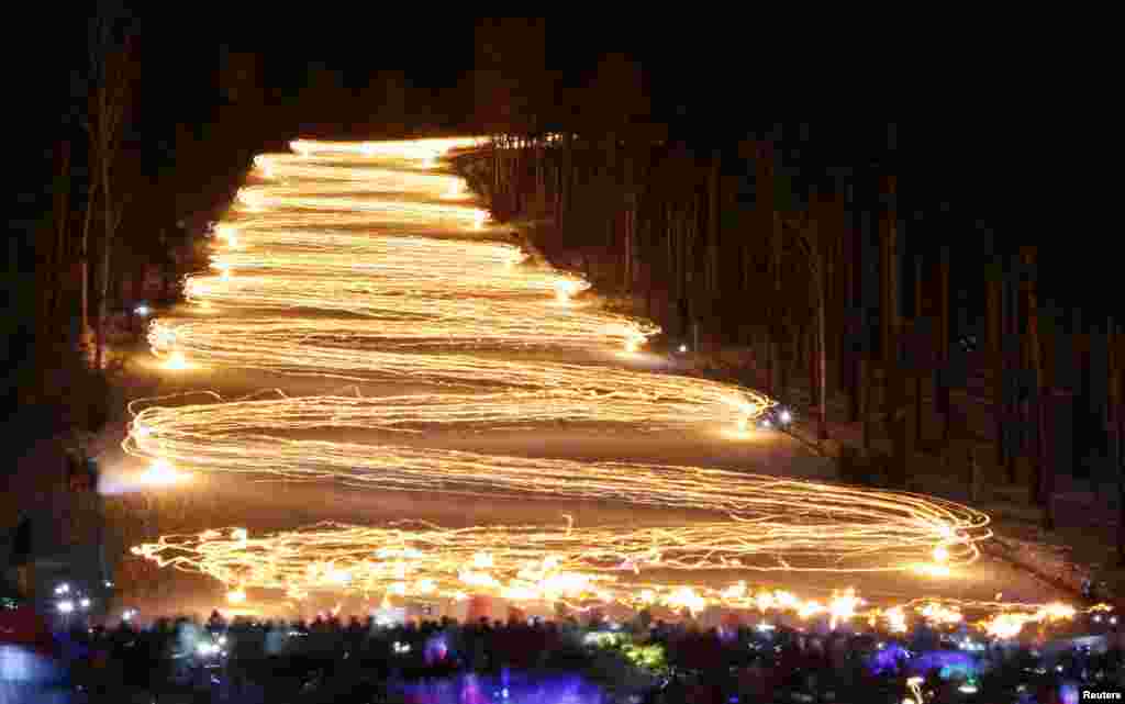 Para penonoton (di bawah) menyaksikan para pemain ski menuruni lereng sambil memegang obor dalam festival obor musim dingin tahunan di kota Zheleznogorsk, sekitar 50 km di sebelah timurlaut kota Krasnoyarsk, Siberia, Rusia.