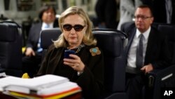 FILE - In this Oct. 18, 2011, file photo, then-Secretary of State Hillary Rodham Clinton checks her Blackberry from a desk inside a C-17 military plane upon her departure from Malta, in the Mediterranean Sea, bound for Tripoli, Libya.
