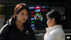 資料照：北京街頭兩名女子站在顯示中國股市走勢的展示板前。 （2024年11月6日）