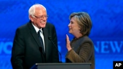 Hillary Clinton, kanan, berbicara pada Bernie Sanders di sela-sela waktu istirahat pada debat calon presiden dari Partai Demokrat, di Saint Anselm College, Manchester, N.H., 19 Desember 2015.