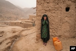 FILE - An Afghan girl warms up her hands as she takes a break from carrying water canisters, in Balucha, Afghanistan, Dec. 14, 2021.