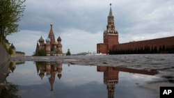 FILE - The Kremlin's Spasskaya Tower, center, and St. Basil's Cathedral, left, reflected in rain water puddles in an empty Red Square during the evening rush hour in Moscow, Russia, May 7, 2020.