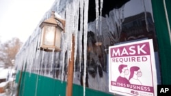 A sign advises patrons of COVID-19 restrictions while long icicles grow from an awning outside a restaurant Feb. 2, 2022, in Denver. 