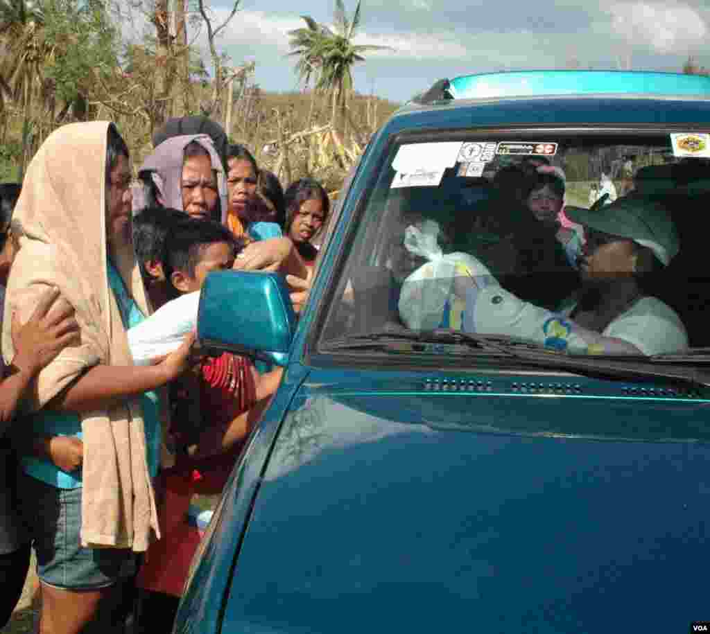A volunteer in a passing car hands out water to typhoon victims, Cebu, Philippines, Nov. 15, 2013. (Steve Herman/VOA)