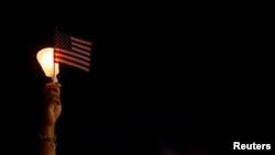FILE - A candle and a U.S. flag are held aloft during a candlelight vigil for one of the 13 U.S. service members killed in the airport suicide bombing in Afghanistan's capital Kabul, in Lawrence, Massachusetts, Aug. 31, 2021. 