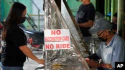 FILE - A woman stands beside a sign to remind passengers to show their vaccination card before riding at a jeepney terminal in Quezon city, Philippines on Jan. 17, 2022.