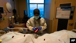 FILE - A nurse attaches a 'COVID Patient' sticker to the body bag of a patient who died of coronavirus at Providence Holy Cross Medical Center in Los Angeles, on Dec. 14, 2021.