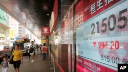 People walk past an electronic board showing the Hong Kong share index outside a local bank in Hong Kong, Monday, Aug. 24, 2015.
