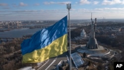 Ukraine's national flag, topped with a trident symbol, flutters above the capital with the Motherland Monument on the right, in Kyiv, Feb. 13, 2022.