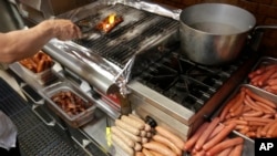 FILE - A cook prepares orders for customers at a gourmet hot dog diner in Chicago, May 7, 2014. A WHO report says eating processed meats such as ham, sausages, bacon and hot dogs can cause cancer.