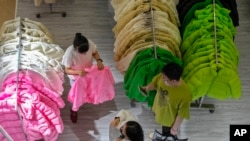 FILE - A woman tries out a fall outfit at a booth doing a promotion sale on clothing a shopping mall in Beijing, Aug. 20, 2023.