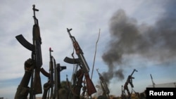 Rebel fighters hold up their rifles as they walk in front of a bushfire in a rebel controlled territory in Upper Nile State, South Sudan, Feb. 13, 2014. 