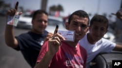 Libyan men hold their elections ID cards while celebrating election day in Tripoli, Saturday, July 7, 2012. 