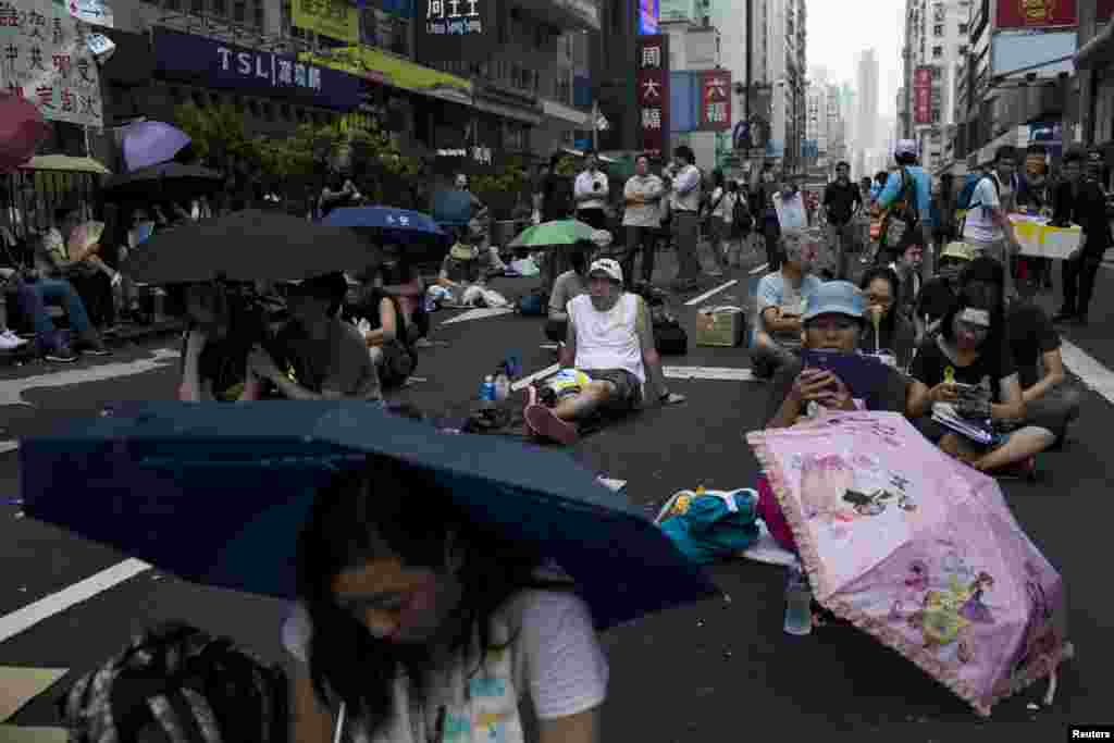 People sit under umbrellas as they attend a rally along a main street at Mongkok shopping district in Hong Kong, Sept. 30, 2014.
