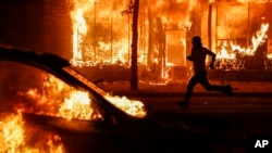 A protester runs past burning cars and buildings on Chicago Avenue, May 30, 2020, in St. Paul, Minn. 