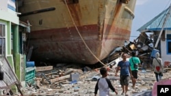 Men walk past Sabuk Nusantara, Oct. 4, 2018, which was swept ashore by the tsunami in Wani village on the outskirt of Palu, Central Sulawesi, Indonesia. The crew of the hulking ferry dropped by the tsunami in front of a row of houses in an Indonesian village say the wave that drove them onto land was a towering 10-15 meters or higher.