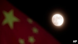 FILE - The moon is seen near a Chinese national flag in Beijing, Dec. 15, 2013. NASA says the U.S. can one day cooperate with China in its space exploration.