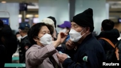A woman wearing a mask to prevent contracting the coronavirus adjusts her husband's mask as they wait to check in at Incheon International Airport in Incheon, South Korea, March 19, 2020.