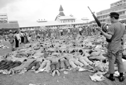 FILE - Police stand guard over Thai student protesters lying on a soccer field at Thammasat University, in Bangkok, Thailand, Oct. 6, 1976.