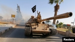 FILE - Militant Islamist fighters on a tank take part in a military parade along the streets of northern Raqqa province.