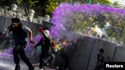 Para demonstran anti-pemerintah melarikan diri seiring penggunaan meriam air oleh polisi anti-huru hara dalam bentrokan dekat markas polisi Bangkok (2/12).