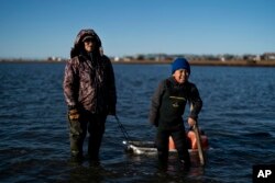 Joe Eningowuk, 62, and his grandson, Isaiah Kakoona, 7, stand for a photo in the lagoon while getting ready for a camping trip in Shishmaref, Alaska, Saturday, Oct. 1, 2022. (AP Photo/Jae C. Hong)