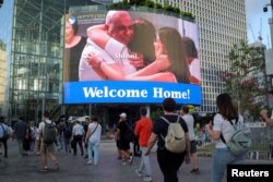 Ljudi hodaju pored video ekrana na kom se vidi Šalom Ziv, koja je bila kidnapovana tokom smrtonosnog napada Hamasa na Izrael 7. oktobra i koju je izraelska vojska oslobodila u Pojasu Gaze, kako se grli sa članovima svoje porodice, 10. juna 2024.