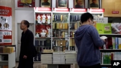 FILE - Customers walk past portraits of Mao Zedong displayed at a bookstore in Beijing. Authorities in China have ordered books by Chinese-American scholar Yu Ying-shih and several others to be removed from sale.