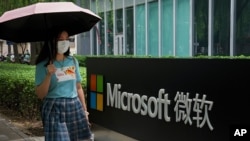 A woman wearing a face mask to help curb the spread of the coronavirus walks by the Microsoft office building in Beijing, July 20, 2021.