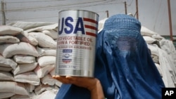 FILE - An Afghan woman carries a container of vegetable oil donated by United States Agency for International Development (USAID), in Kabul, Afghanistan, July 26, 2011.