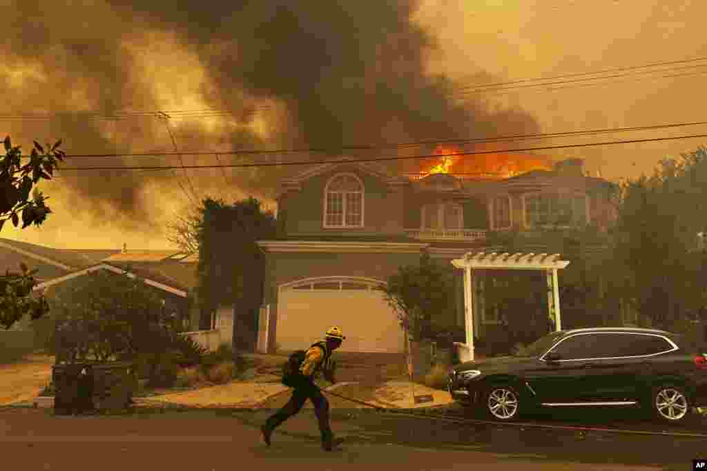 A residence burns as a firefighter battles the Palisades Fire in the Pacific Palisades neighborhood of Los Angeles, Jan. 7, 2025.