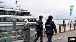 Petugas kepolisian yang sedang berpatroli melintas di depan seorang perempuan yang mengenakan hijab di Zell am See, Austria, 1 Oktober 2017. 