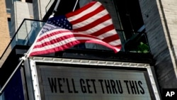 FILE - A man wearing face mask walks past a bank electronic board showing the Hong Kong share index at Hong Kong Stock Exchange, April 14, 2020. 