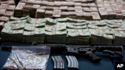 FILE - An assault rifle, and bundles of U.S. dollars and Mexican pesos are displayed in Mexico City, Mexico, June 15, 2012. 