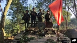 FILE - Members of the Myanmar National Democratic Alliance Army hold the group's flag as they pose for a photograph on a captured army armored vehicle in Myanmar, Oct. 28, 2023.