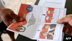 Seorang petugas tempat pemungutan suara (TPS) memberikan surat suara kepada seorang pemilih di TPS di Kuta, Bali, saat pelaksanaan pilkada, 9 Desember 2015. (Foto: AFP)