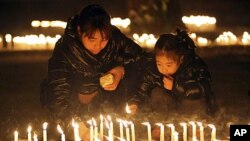 A man and a child light candles during a vigil to honor a Chinese father and his baby shot dead by thieves, in Rome, January 10, 2012.