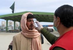 FILE - A health worker takes the temperature of a man, who returned from Afghanistan, following the coronavirus outbreak, outside a medical camp near the Friendship Gate, at the Pakistan-Afghanistan border town of Chaman, Pakistan, Feb. 26. 2020.