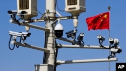 FILE - A Chinese national flag flutters near surveillance cameras mounted on a lamp post in Tiananmen Square in Beijing, March 15, 2019. 
