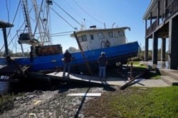 Boat owner Ricky Mitchell, left, surveys damage to his boat that Hurricane Zeta washed up against a home in Lakeshore, Miss., Oct. 29, 2020.