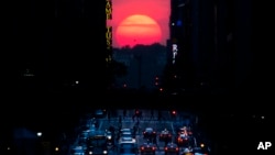 FILE - The sun sets along 42nd Street in Manhattan during an annual phenomenon known as "Manhattanhenge," when the sun aligns perfectly with the city's transit grid, Wednesday, May 29, 2013, in New York. (AP Photo/John Minchillo, File)