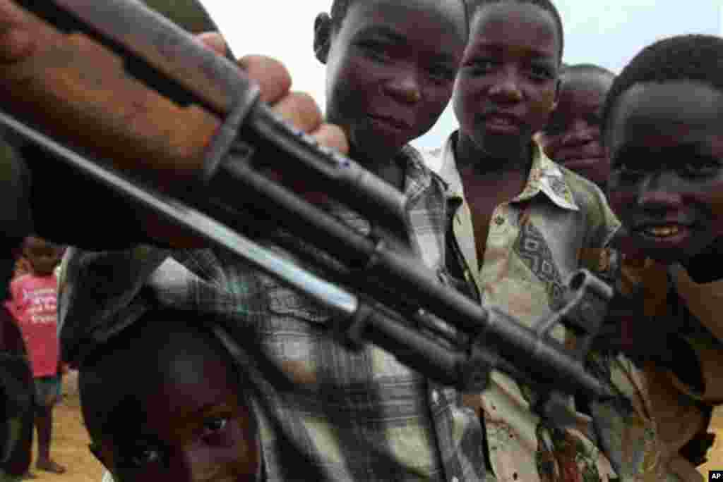 Des enfants s'approchent d'un homme armé en RDC. Au Congo, des dizaines d'enfants abandonnés dans la rue, sont exposés aux armes et sont parmi les premières vicitimes des bavures policières dénoncées. (AP Photo/John Bombengo). 