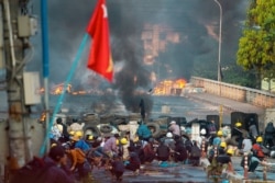 FILE - Anti-coup protesters take cover at a barricade as they clash with security forces on Bayint Naung Bridge in Mayangone, Yangon, Myanmar, March 16, 2021.