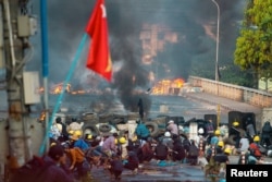 FILE - Anti-coup protesters take cover at a barricade as they clash with security forces on Bayint Naung Bridge in Mayangone, Yangon, Myanmar, March 16, 2021.