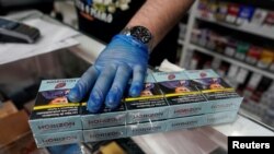 An employee of a tobacco shop sells a pack of cigarettes at the Vallecas neighborhood, in Madrid, Spain March 13, 2020.