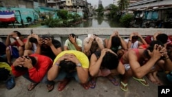 FILE - Filipino men place their hands over their heads as they are rounded up during a police operation as part of the continuing "War on Drugs" campaign of Philippine President Rodrigo Duterte in Manila, Philippines. 